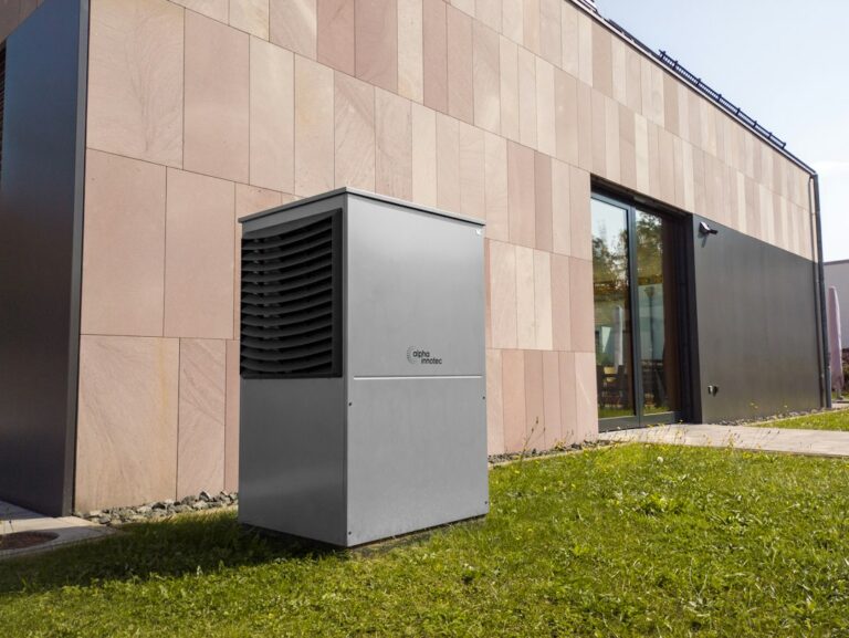 Outdoor heat pump condenser unit sitting on the ground beside a modern home